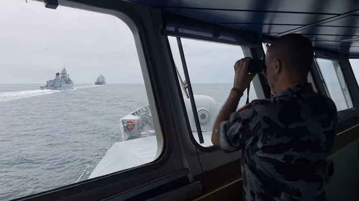 Een opvarende van het Ierse marineschip LE WIlliam Butler Yeats kijkt door een verrekijker naar de navigatieoefening..