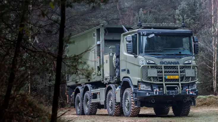 Een donkergroene Scania Gryphus-truck rijdt door een beboste omgeving. Achterop staat een container.