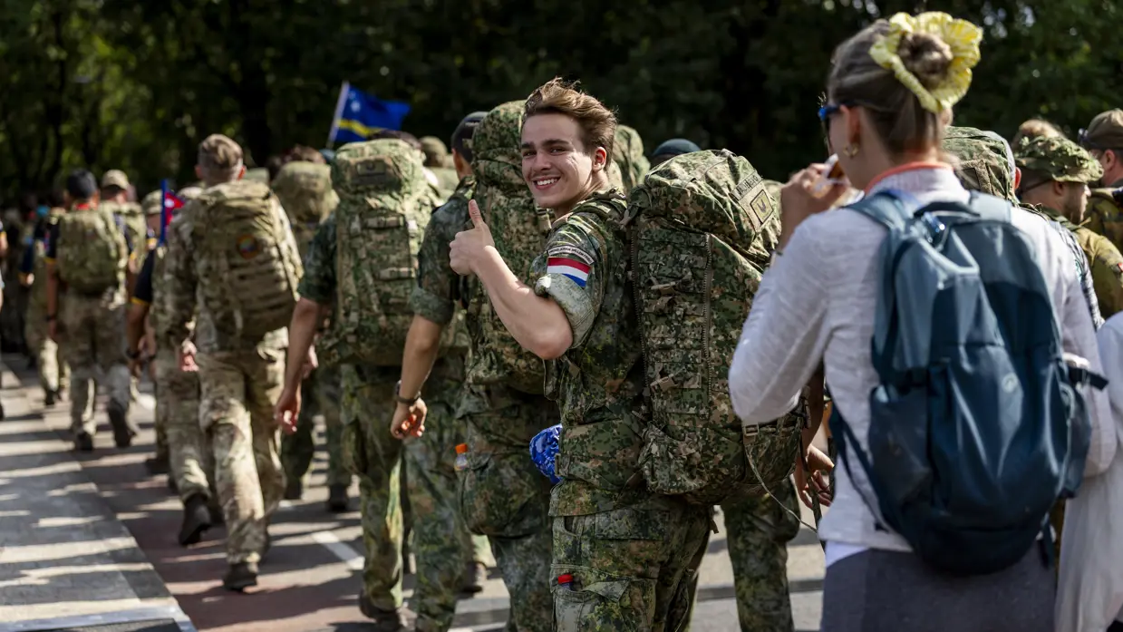 Een groep wandelende militairen op de rug gezien, eentje draait zich om en steekt een duim omhoog.
