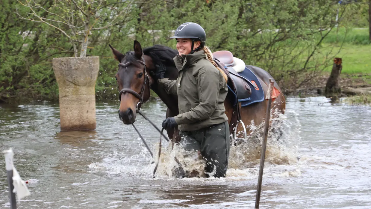 Een glimlachende vrouw met een helm op leidt met de teugels in de hand haar paard door het water (links) en (rechts) dezelfde vrouw springt met haar paard over een hindernis.