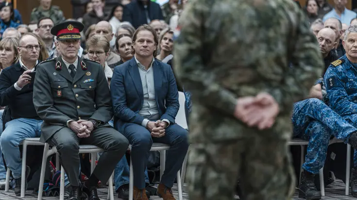 Staatssecretaris Gijs Tuinman zit op een stoel. Voor hem op de rug gezien een militair. 
