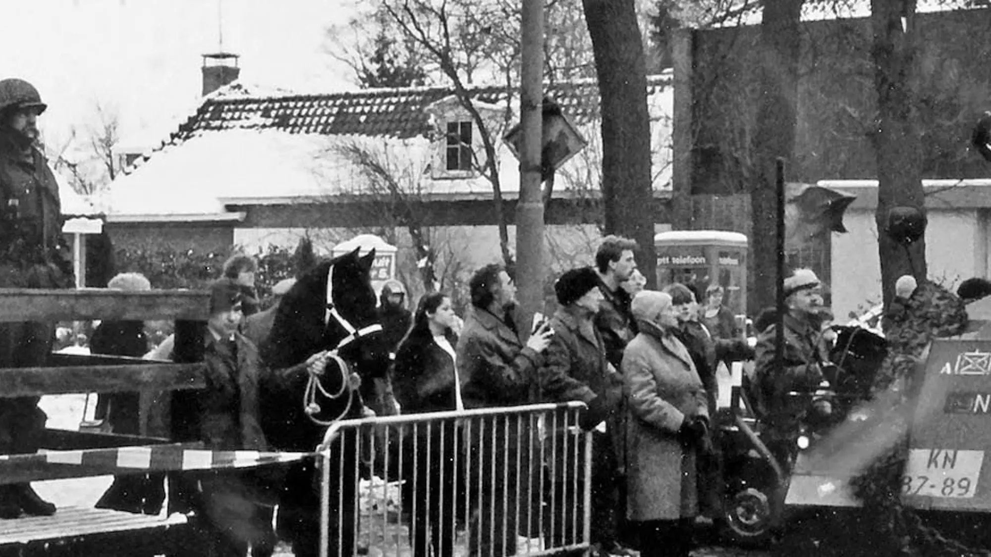 Oude foto van een rijdende tank met publiek achter een dranghek.