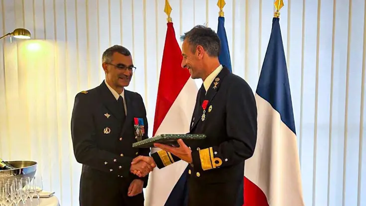 Vice-admiraal Jan Willlem Hartman en generaal Gaël Diaz de Tuesta schudden elkaar de hand. Op de achtergrond zijn de vlaggen van de twee landen te zien