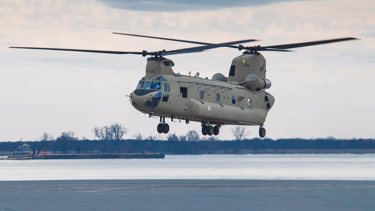 Militaire transporthelikopter hangt vlak boven de grond.