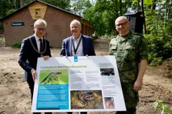 3 mannen voor een Faunahuis. In hun handen een groot bord met informatie over het Faunahuis op de Bernhardkazerne