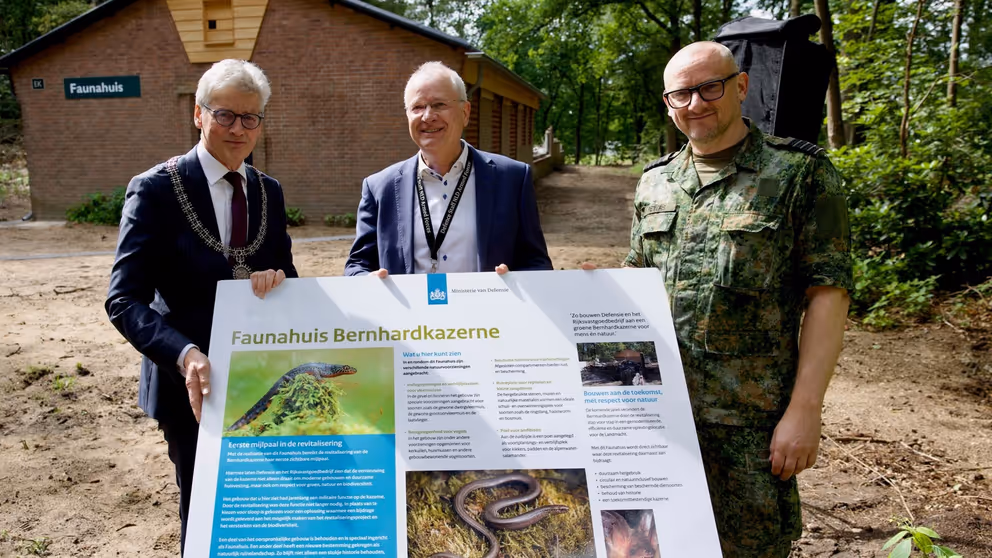 3 mannen voor een Faunahuis. In hun handen een groot bord met informatie over het Faunahuis op de Bernhardkazerne