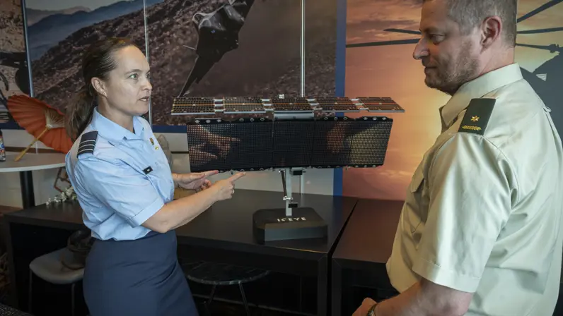 Luitenant-kolonel Petra Wijnja in gesprek met liaison-officer van de landmacht bij een model van een SAR-satelliet van het Finse ICEYE
