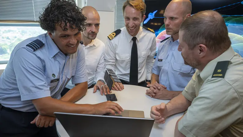 Groepsfoto van enkele militairen en burgers met in een midden een model van een satelliet.