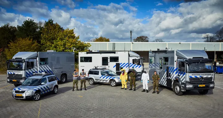 Militairen in vlekkenpak en beschermende pakken en wagens.