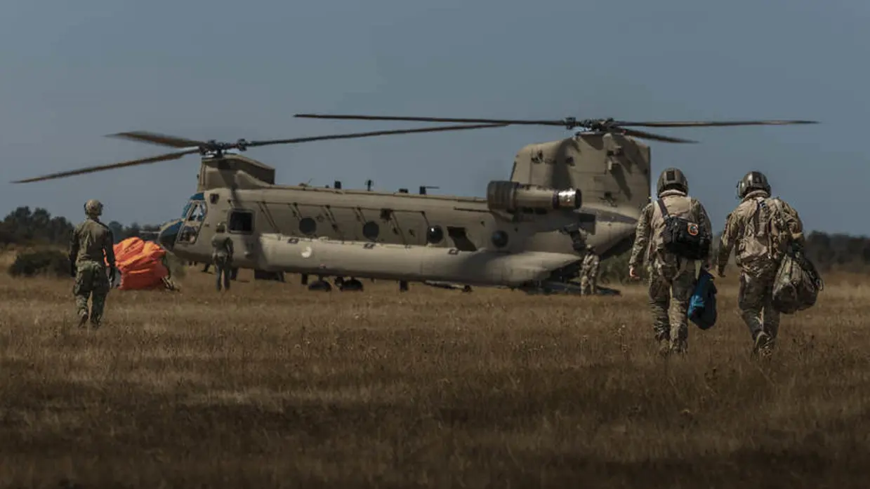4 militairen op de rug gezien lopen naar een Chinook-transporthelikopter.