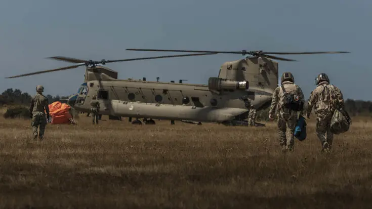4 militairen op de rug gezien lopen naar een Chinook-transporthelikopter.
