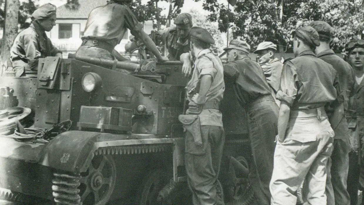 Groep militairen overlegt bij een pantservoertuig.
