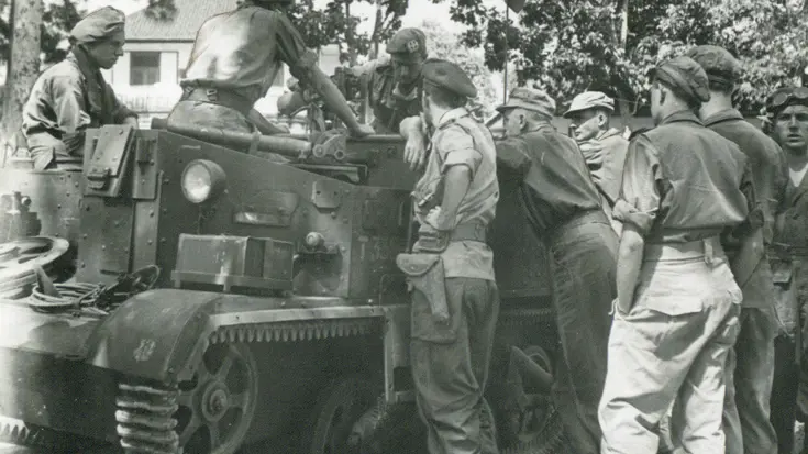 Groep militairen overlegt bij een pantservoertuig.