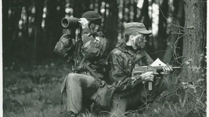 Militairen in bos. 1 met wapen en 1 met verrekijker.