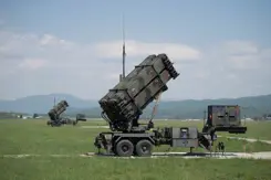 2 Patriot-luchtverdedigingssystemen op grasland met heuvellandschap op de achtergrond.