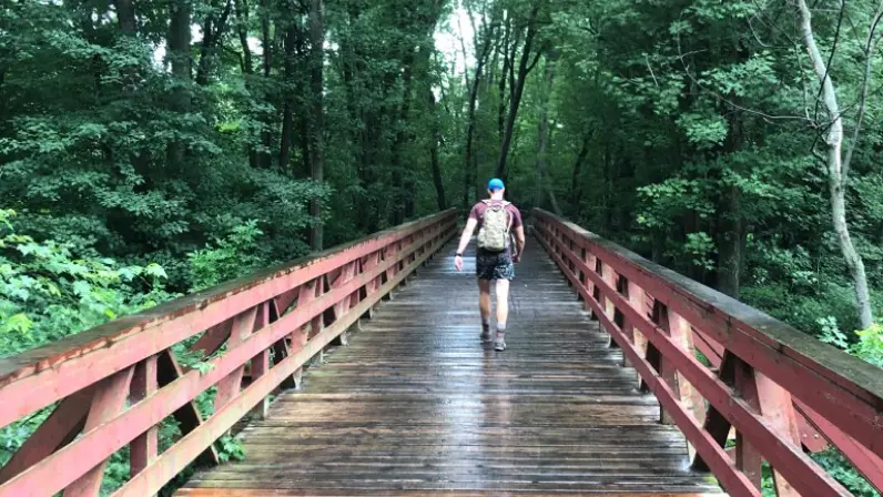 Een man loopt over een houten brug met een rugzak op