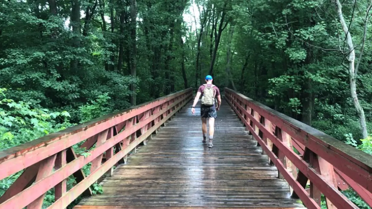 Een man loopt over een houten brug met een rugzak op