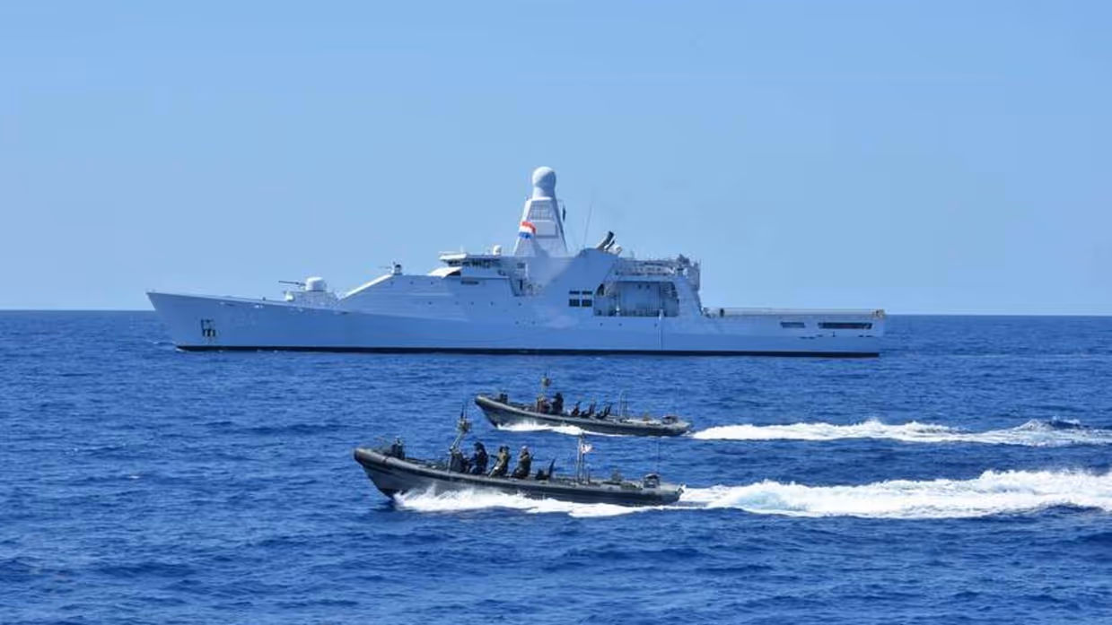 Een marineschip op zee, geflankeerd door snelle onderscheppingsboten.