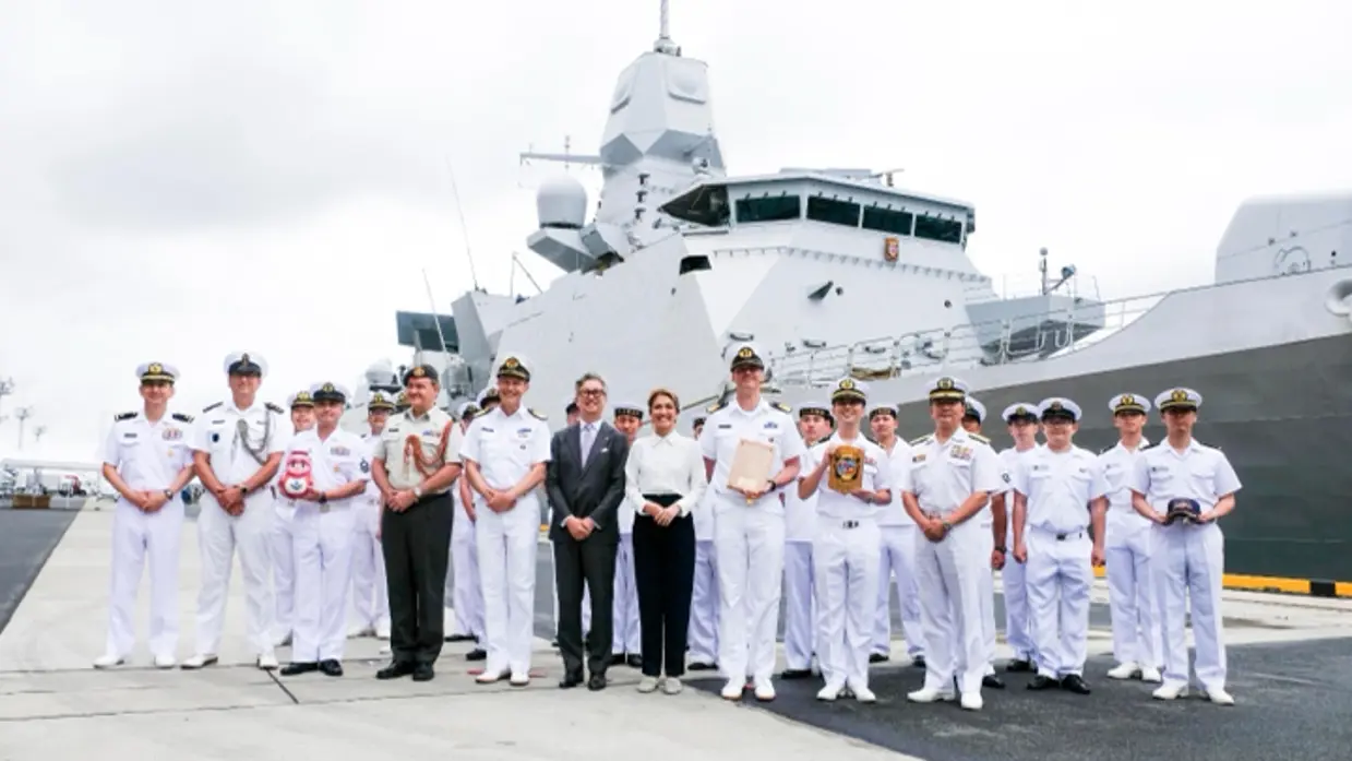 De ministers staan op een kade tussen Japanse mariniers, met daarachter het schip.