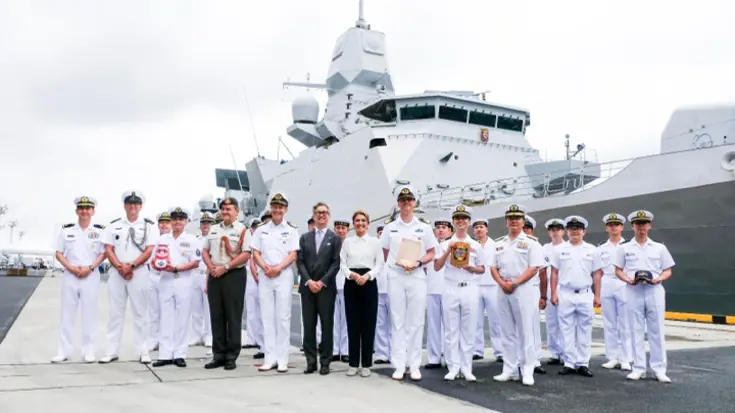 De ministers staan op een kade tussen Japanse mariniers, met daarachter het schip.