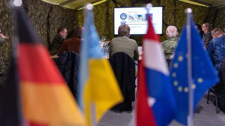 Vlaggetjes van Duitsland, Nederland, Europa en Oekraïne op een bureau in een legertent.
