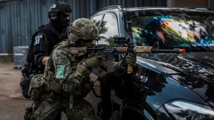 Agent en militair bukken naast een auto.