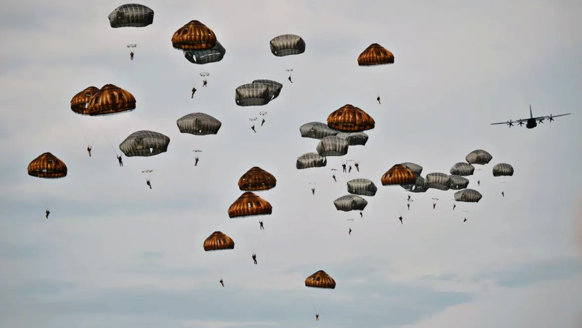 Tientallen militairen hangen onder hun geopende parachutes nadat ze net uit een vliegtuig zijn gesprongen.