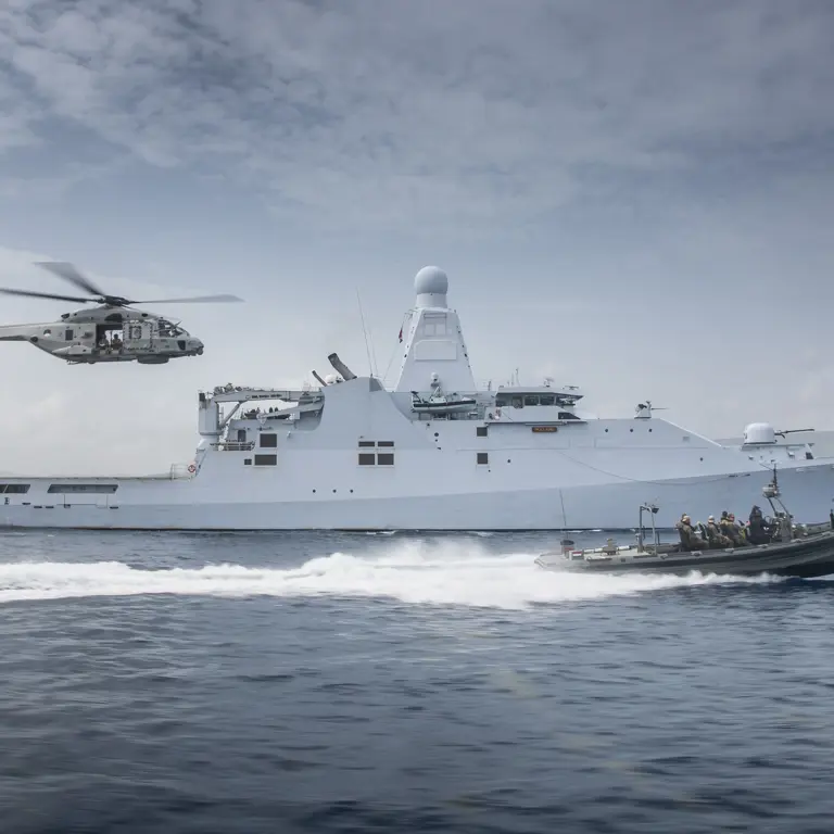 Schip op zee met boot die er naast vaart en een helikopter volgt.