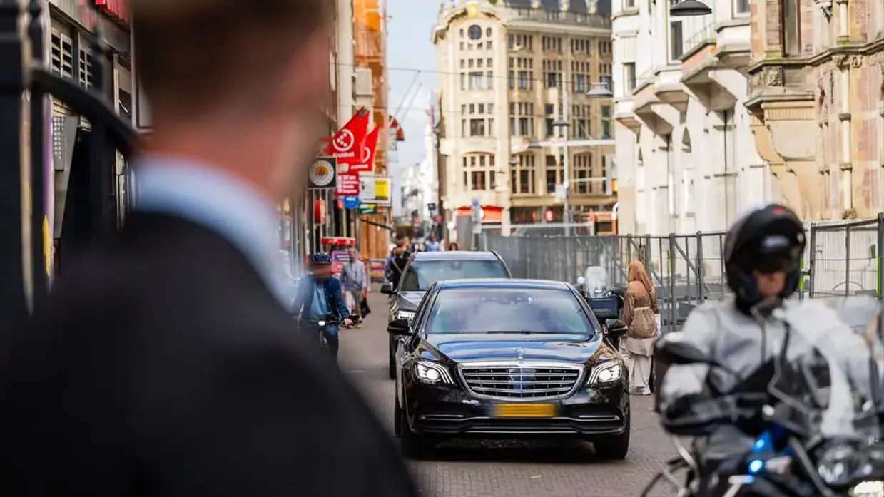 Een beveiliger op de voorgrond kijkt naar aankomende auto’s in de binnenstad.