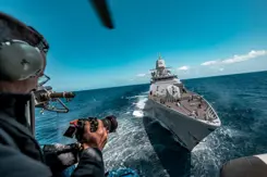 Een marinier kijkt vanaf zijn schip naar zijn camera. Voor hem ligt een ander schip.