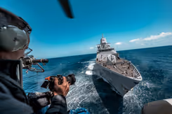 Een marinier kijkt vanaf zijn schip naar zijn camera. Voor hem ligt een ander schip.