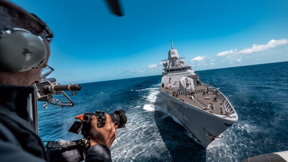 Een marinier kijkt vanaf zijn schip naar zijn camera. Voor hem ligt een ander schip.