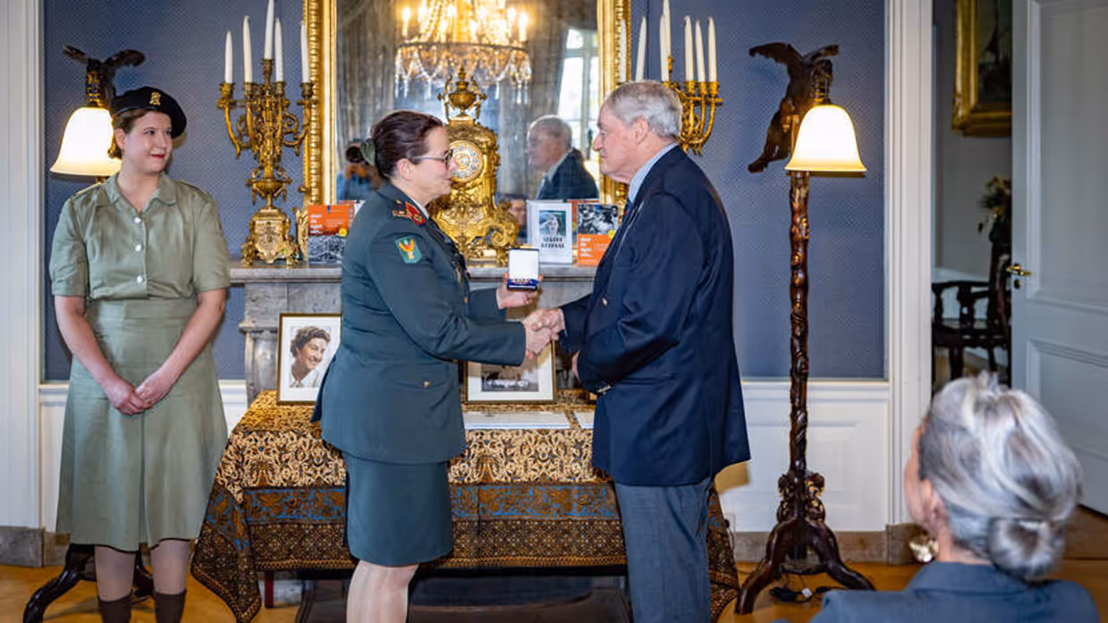 Militair overhandigt nabestaande onderscheiding.