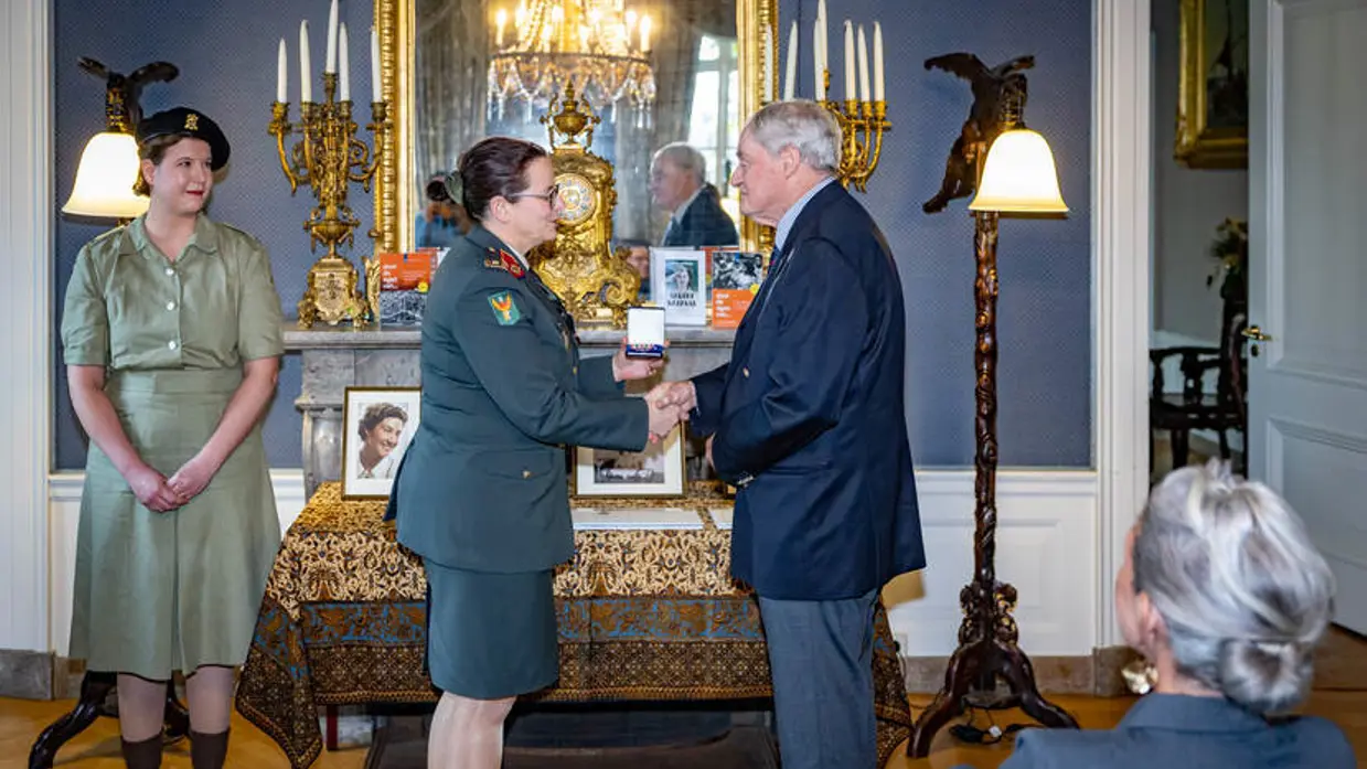 Militair overhandigt nabestaande onderscheiding.