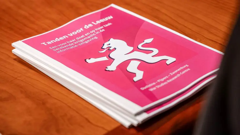 Stapeltje rapporten met rode kaft en afbeelding witte leeuw op houten tafel.