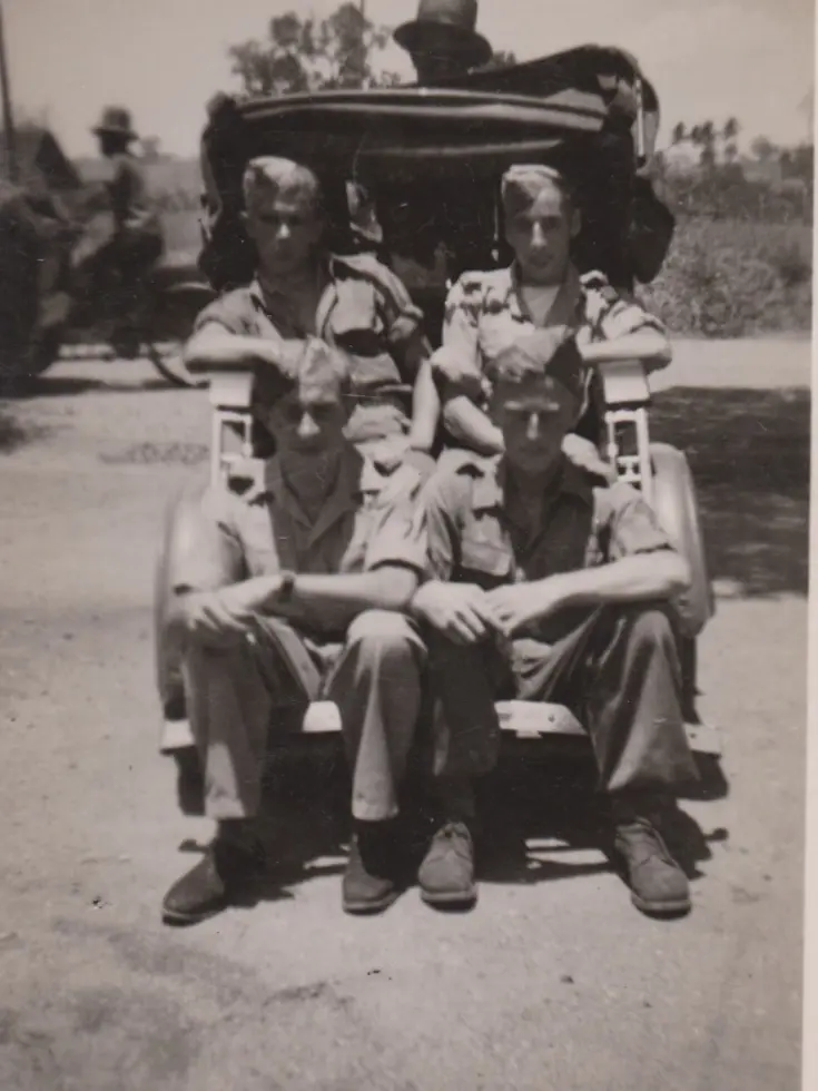 Oude foto met 4 militairen zittend op de achterkant van een auto.