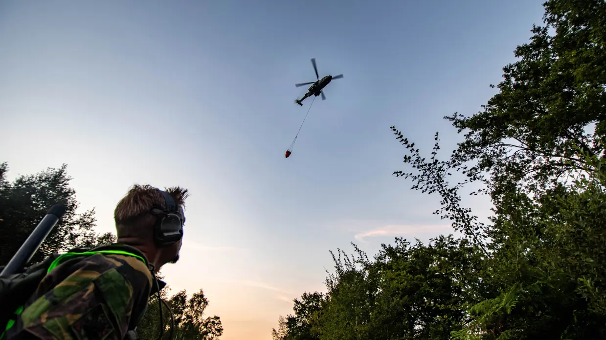 Een militair kijkt omhoog naar een helikopter met een bambi bucket.