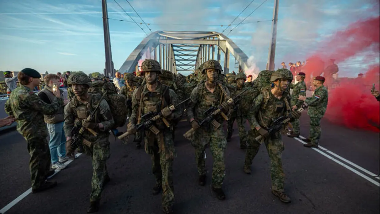 Militairen in volle bepakking marcheren over brug.
