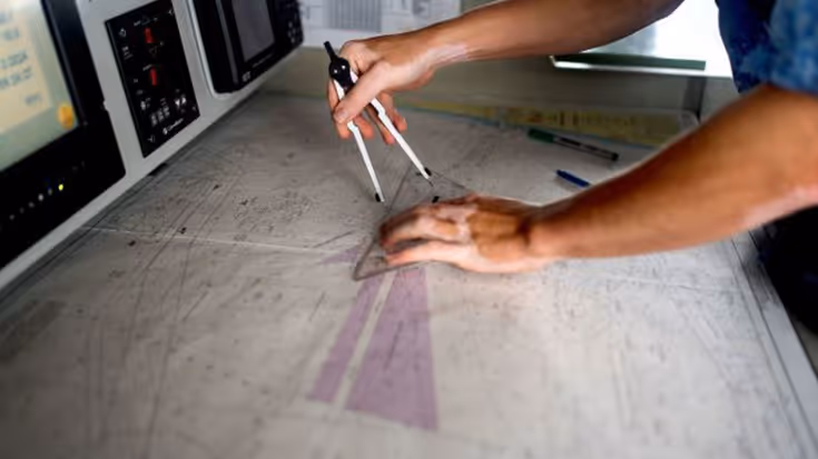 Een marinier is aan het werk met een kaart, een passer en een geodriehoek. 