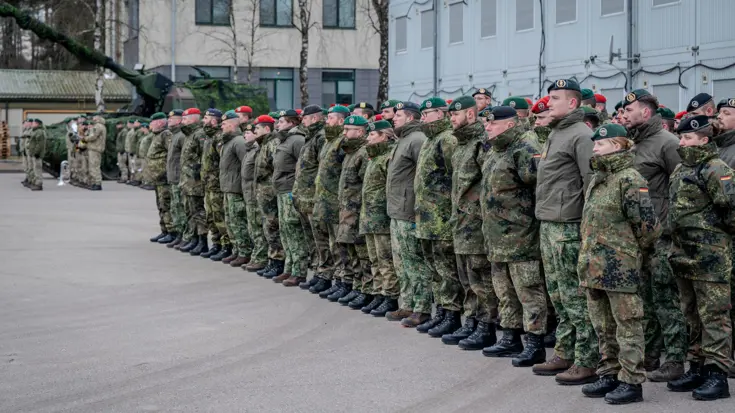 Groep militairen in de houding op binnenplaats. Een tank staat op de achtergrond.