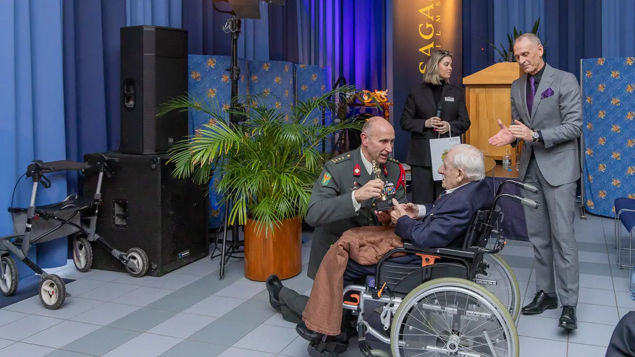 Alttekst = Veteraan Ton Hazeleger ontvangt een Oscarbeeld uit handen van de commandant van Bronbeek. 