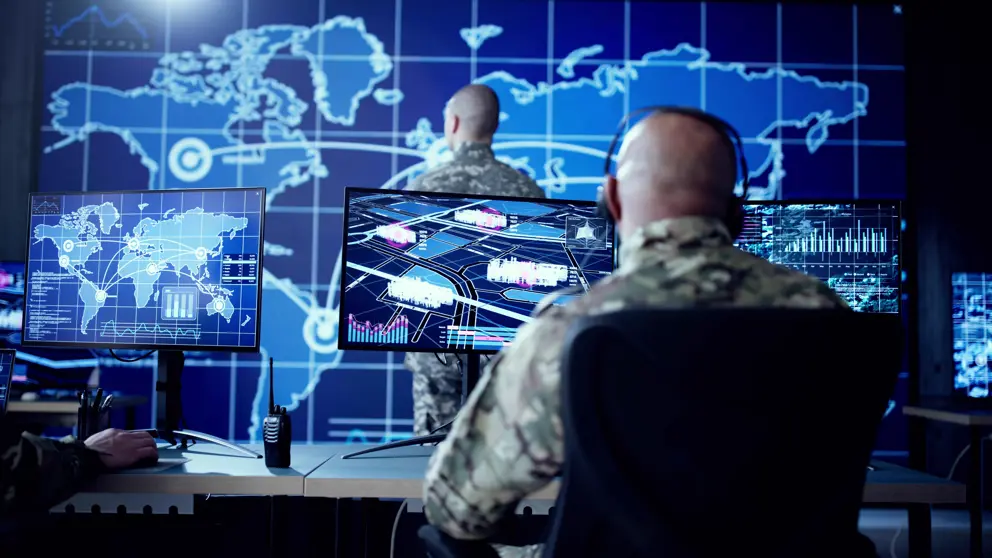 Militairen zitten achter beeldschermen waar de wereldkaart op staat.