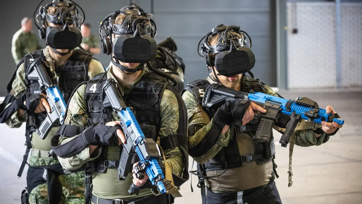 3 landmachtmilitairen  in camouflagepak met VR-bril en wapen.