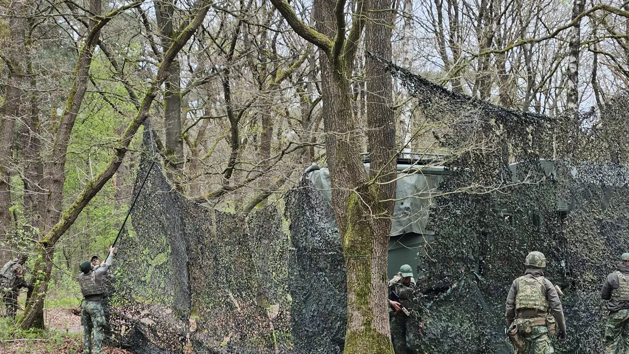 Militairen plaatsen een camouflagenet over boomtoppen.
