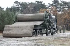 Wegenmattenlegger staat geparkeerd aan rand van bos.