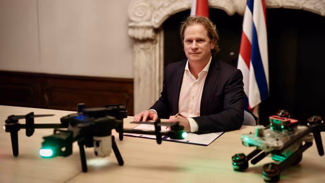 Staatssecretaris Tuinman zit achter de tafel waar 2 drones op staan.