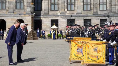 Koning Willem-Alexander en de bondspresident van Duitsland, Frank-Walter Steinmeier, buigen voor in rijen opgestelde militairen gekleed in ceremonieel tenue. Drie van hen steken oranje vaandels naar hen uit.