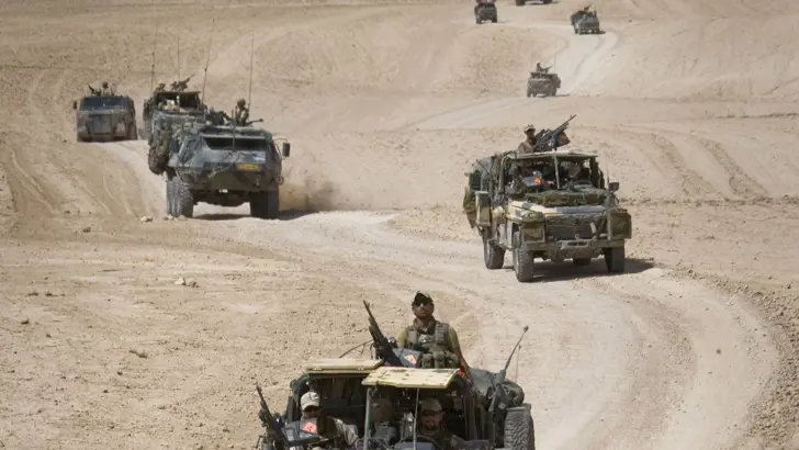 Militairen rijden door woestijn in Afghanistan.