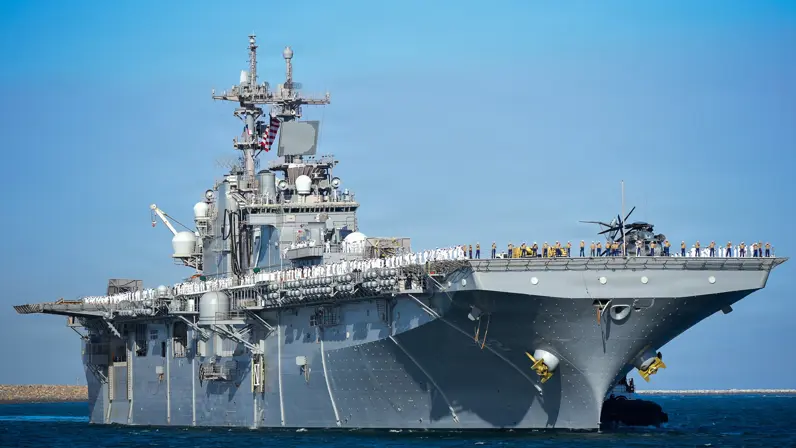 U.S. Coast Guard, Chief Petty Officer Lisa Ferdinando  Alt-tekst: De USS Essex op zee met de bemanning in de houding aan dek. 