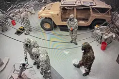 5 militairen met gasmaskers in een ruimte met een voertuig.